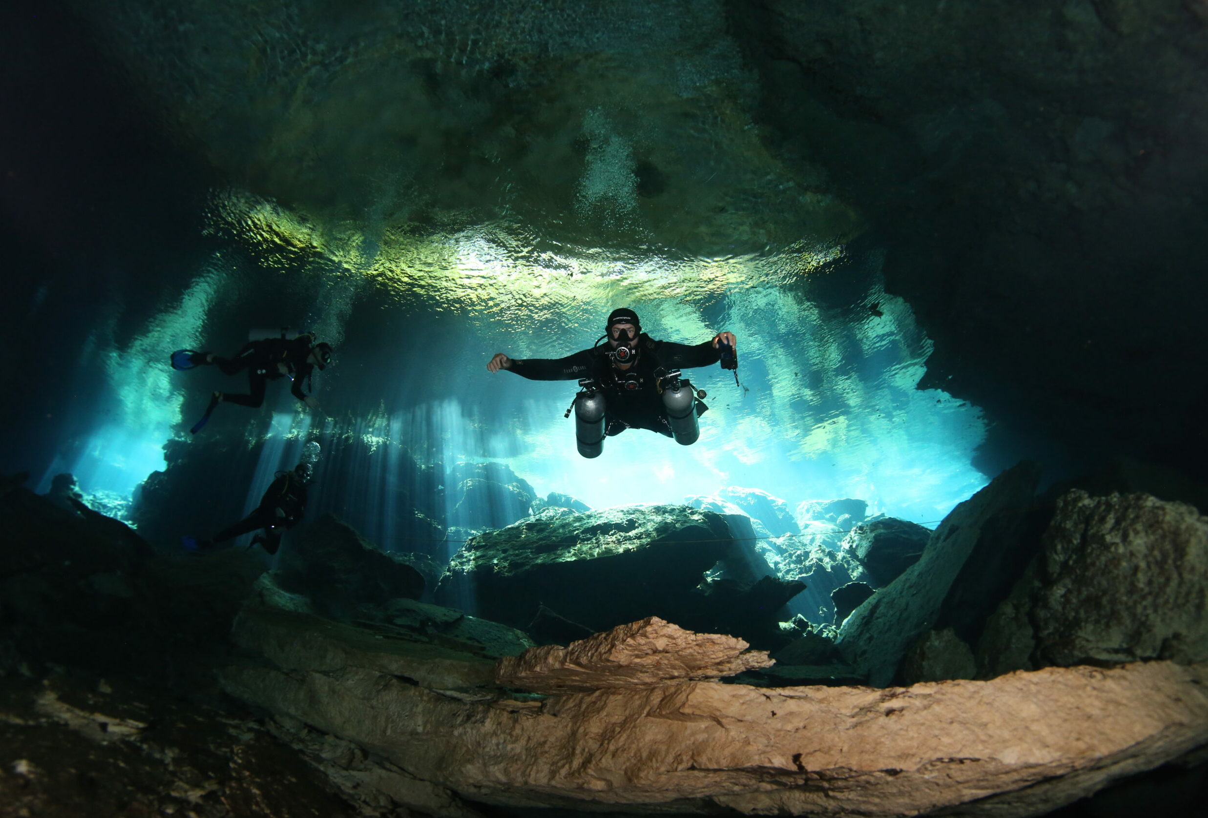 Scuba divers from Triton Diving experience the ethereal light beams of an underwater cave in Playa del Carmen
