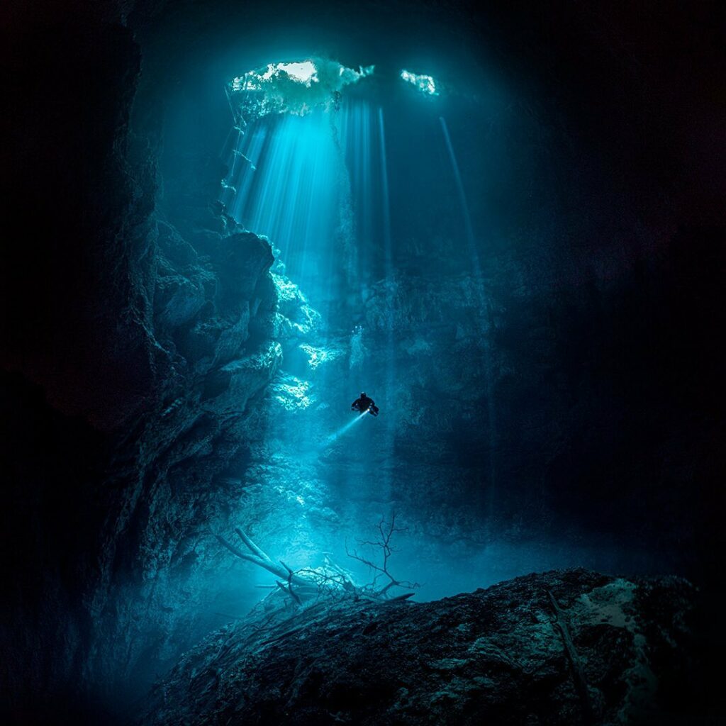 Plongeur solitaire éclairé par les rayons du soleil dans la grotte sous-marine connue sous le nom de The Pit, avec Triton Diving