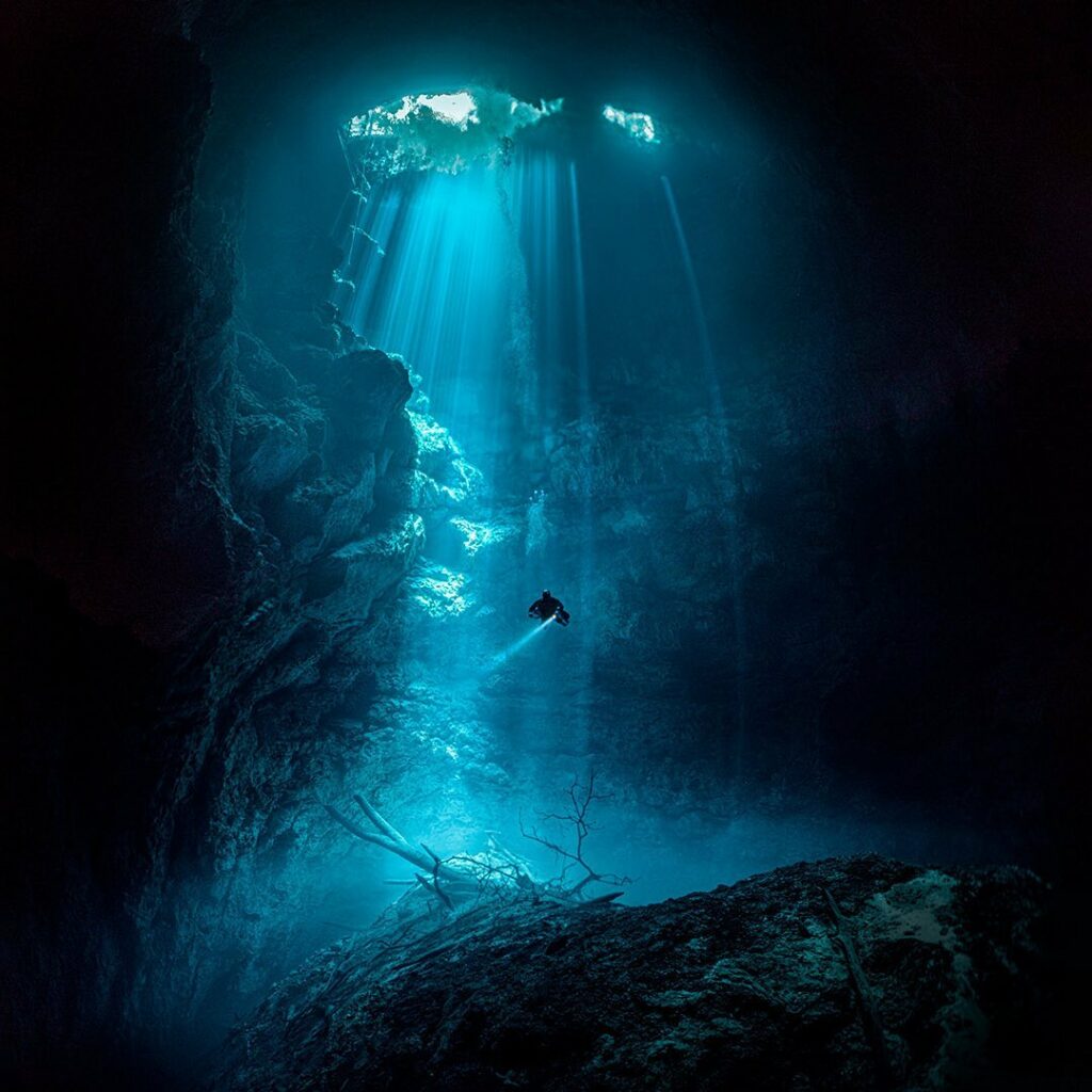 Solo diver illuminated by sunbeams in the underwater cave known as The Pit, with Triton Diving