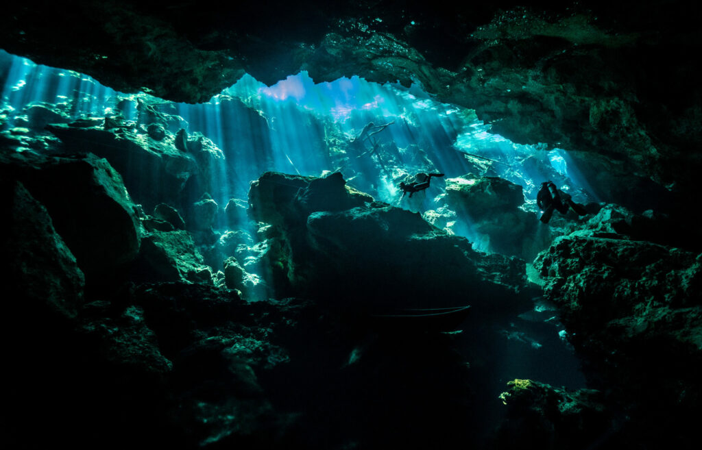 Des plongeurs sous-marins explorent les cavernes sous-marines du cénote Chac Mool éclairées par des faisceaux de lumière céleste.