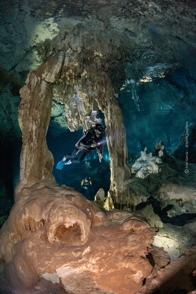 Plongeur de Triton Diving encadré par un arc naturel de calcaire dans les eaux turquoise du Cénote Dos Ojos