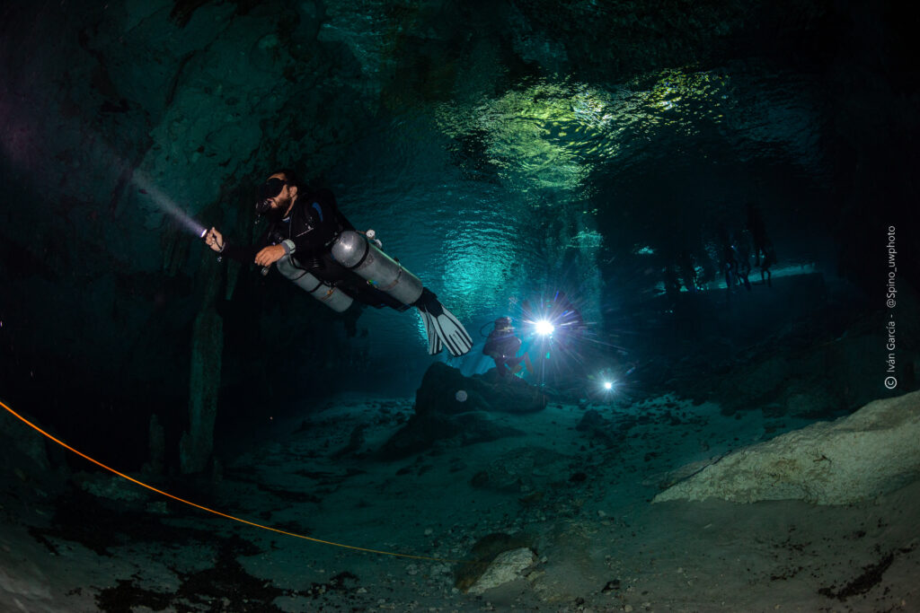L'équipe de Triton Diving navigue habilement dans les eaux claires du Cénote Dos Ojos, avec des faisceaux de lumière éclairant le chemin
