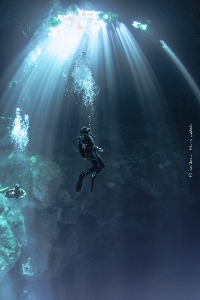 Explorateur de Triton Diving suspendu au milieu des rayons de soleil dans le bleu profond du Cenote The Pit