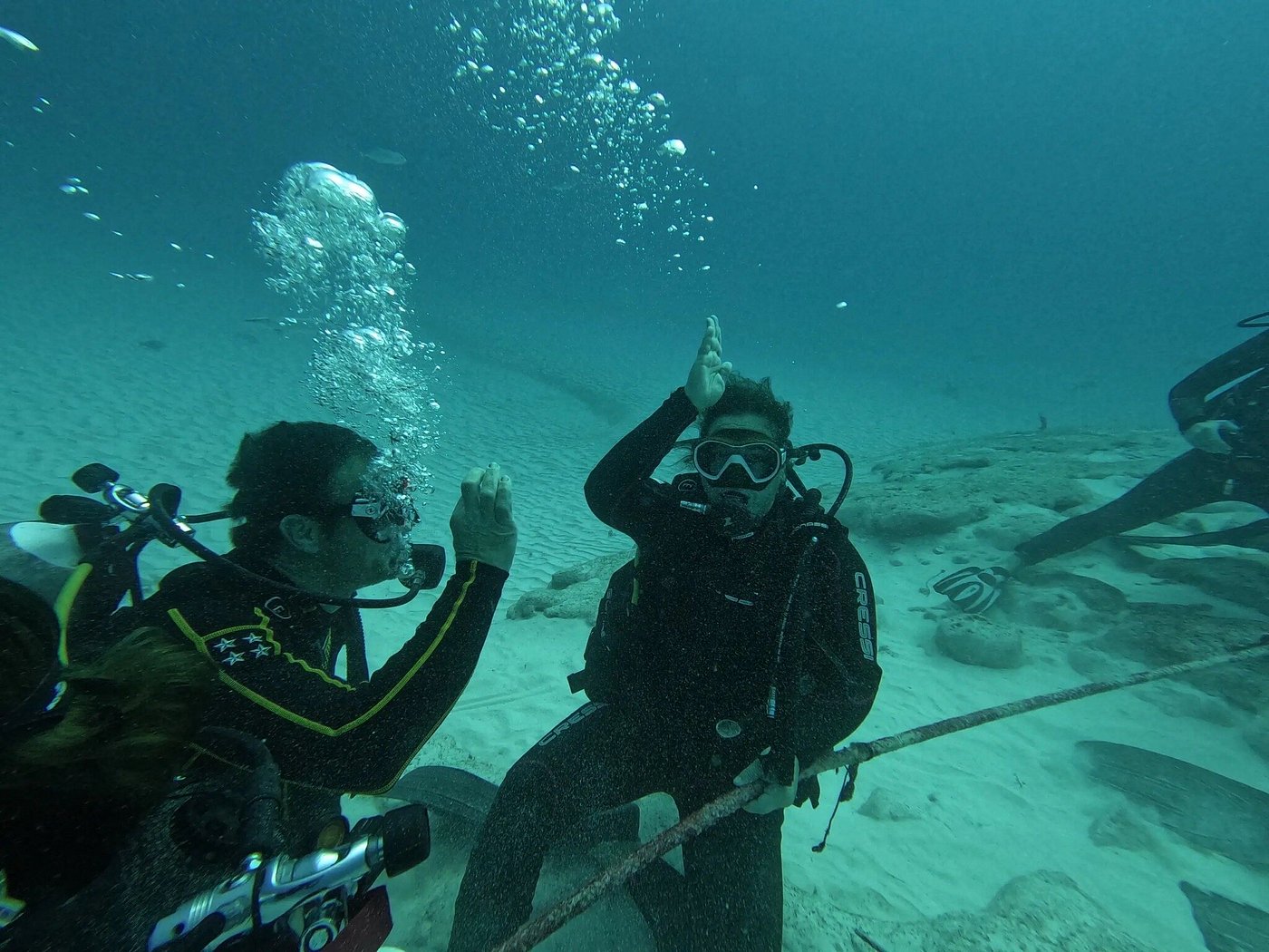 Deux plongeurs sous-marins faisant des signaux de requin au-dessus d'un fond marin sablonneux.