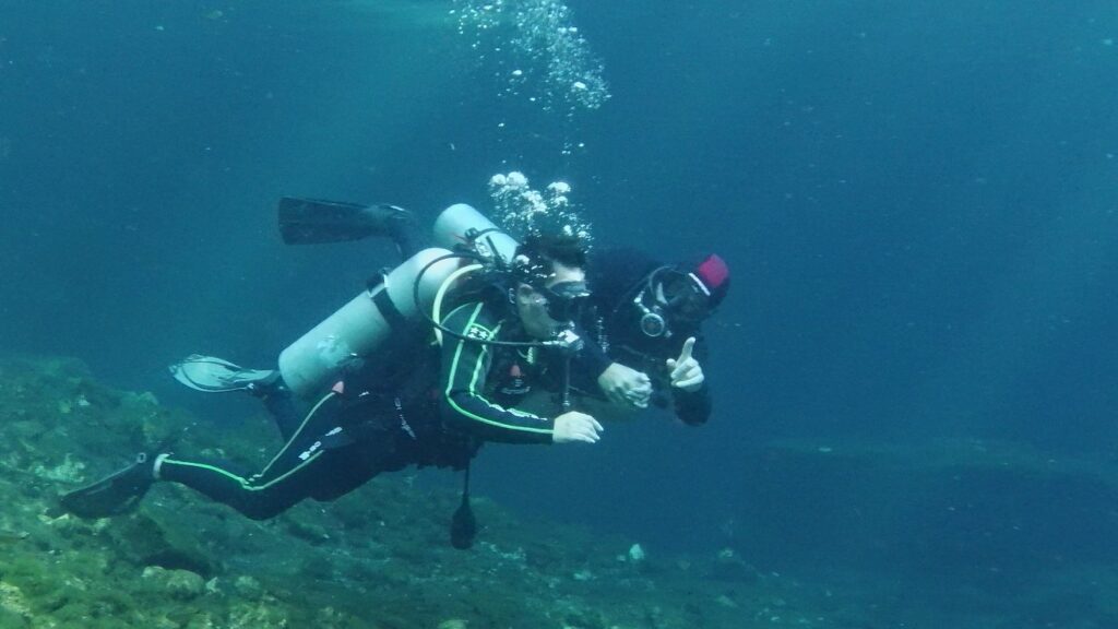 Two divers practicing underwater hand signals during a Triton diving lesson.