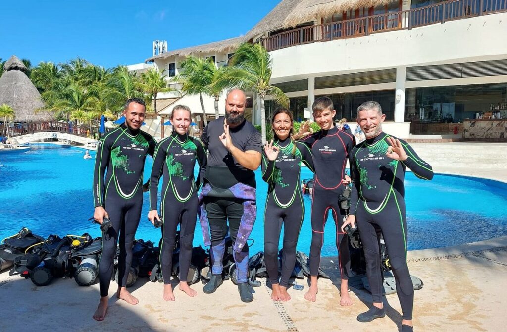 Group of happy divers in Triton wetsuits by the pool after a diving lesson.