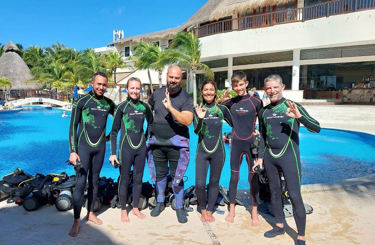 Groupe de plongeurs souriants en combinaisons Triton au bord de la piscine après une leçon de plongée.