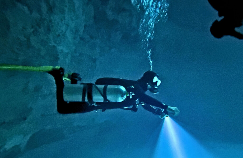 Diver with a torch along the wall of Cenote Maravilla
