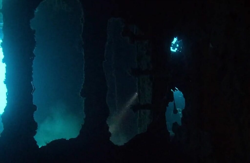 Intérieur de l'épave C-56, un plongeur avec sa lampe, à Puerto Morelos