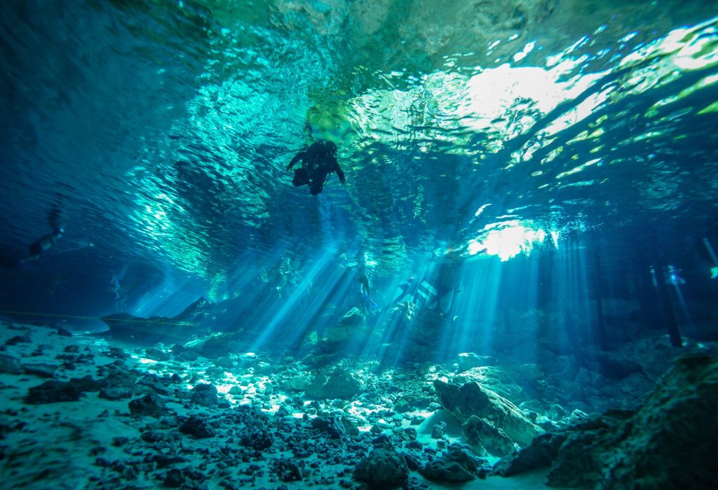 Plongeur sous les rayons de soleil du cénote Dos Ojos