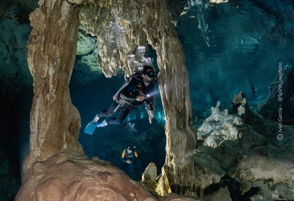 Triton Diving diver framed by a natural limestone arch in the turquoise waters of Cenote Dos Ojos